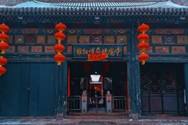 Traditional Chinese doorway decorated with red lanterns and gold Chinese signboard, teal walls, and carved panels above the entrance.