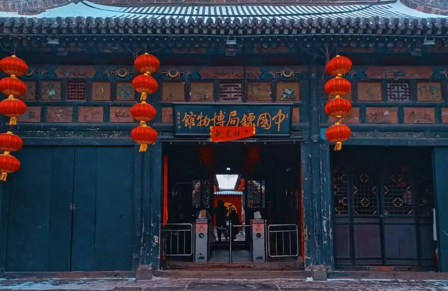 Pingyao Museum,Pingyao,Chinatour Traditional Chinese doorway decorated with red lanterns and gold Chinese signboard, teal walls, and carved panels above the entrance.