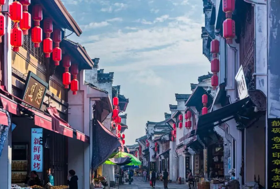 Huizhou Ancient City,Huangshan,Chinatour Narrow Chinese street lined with red lanterns, traditional shopfronts, and pedestrians walking along the walkway.