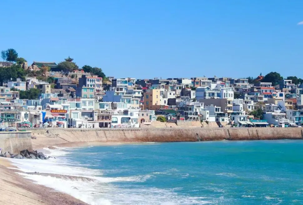 Dongshan Island,Zhangzhou,Chinatour Coastal town with white buildings along a seawall and turquoise water under a clear blue sky, by the shore.