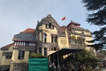Former German Governor’s Mansion ,Qingdao,Chinatour Historic building with stone masonry, yellow walls, red-tiled roofs and a flag on top under a clear blue sky