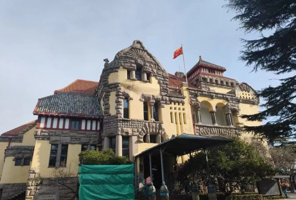 Former German Governor’s Mansion ,Qingdao,Chinatour Historic building with stone masonry, yellow walls, red-tiled roofs and a flag on top under a clear blue sky