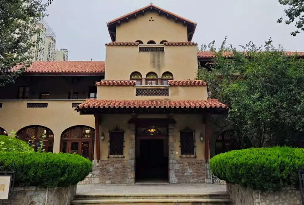 Former Residence of Puyi Jingyuan Garden,Tianjin,Chinatour Villa-style building with red-tiled roof, arched windows, and a central entrance framed by trimmed hedges in a garden setting.