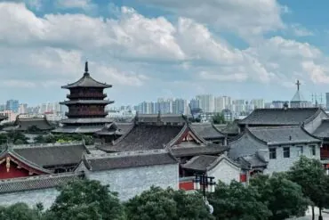 Pingcheng Ancient Town,Datong,Chinatour Traditional Chinese temple complex with a multi-tier pagoda in the foreground and a modern city skyline in the distance under a blue sky.
