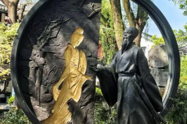 Shen Garden ,Shaoxing,Chinatour Circular sculpture featuring a gold-toned seated female figure and a dark-robed man in a garden setting, with a large circular frame surrounding them.