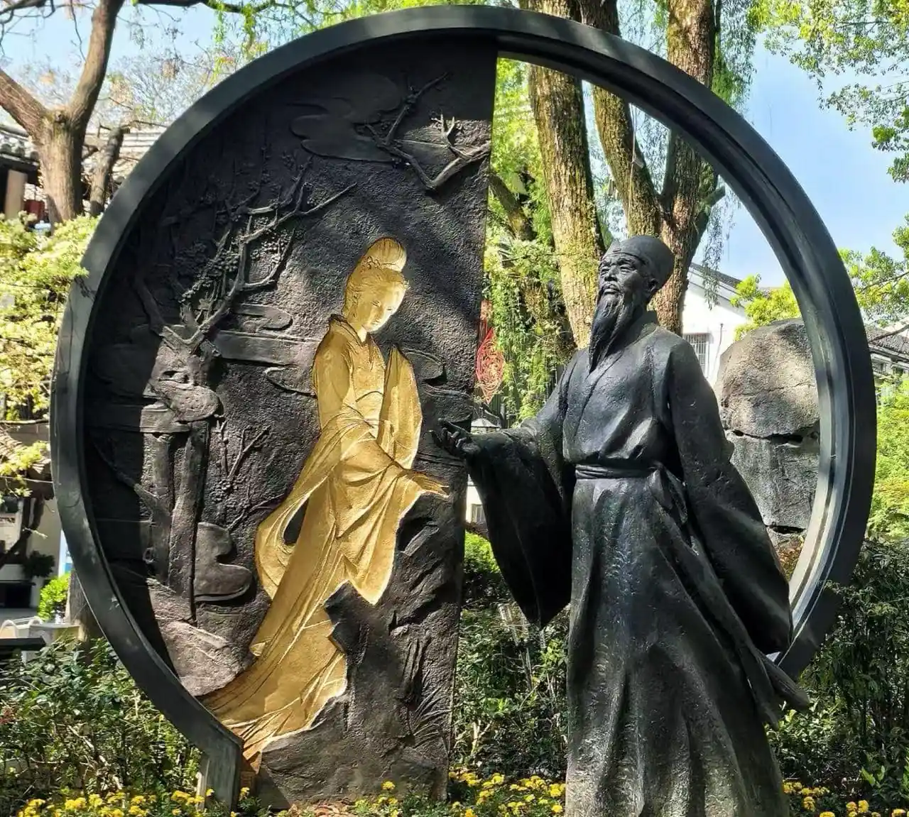 Shen Garden ,Shaoxing,Chinatour Circular sculpture featuring a gold-toned seated female figure and a dark-robed man in a garden setting, with a large circular frame surrounding them.