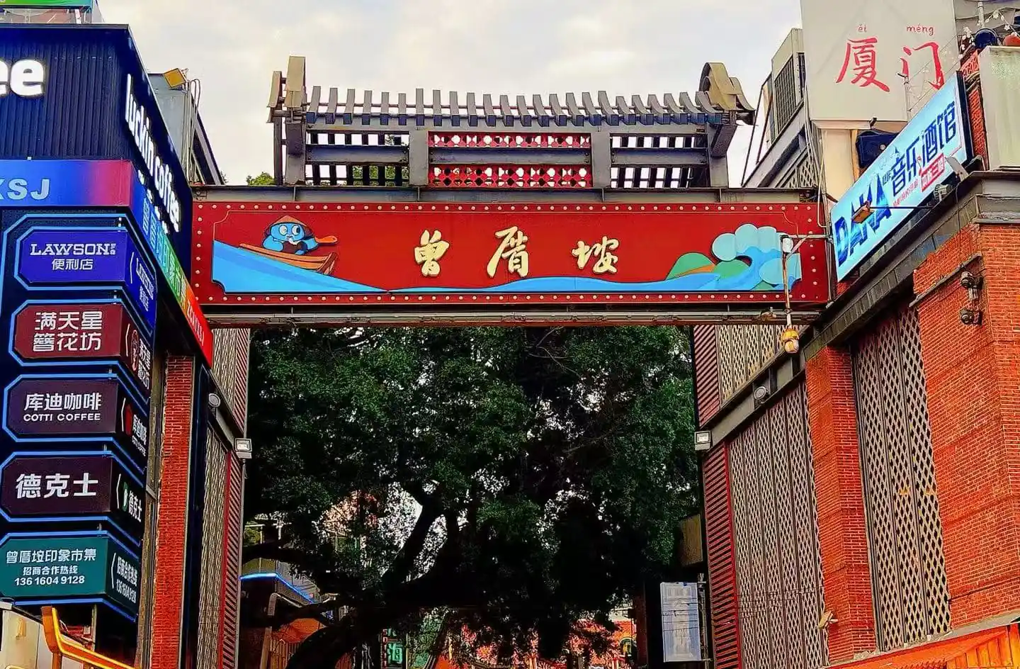 Zengcuoan Coastal Art Village,Xiamen,Chinatour Decorative red gate over a street with Chinese characters, flanked by colorful signs; cartoon penguin in a blue boat on the left.