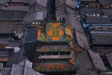 Aerial view of a historic Chinese temple with a bright multicolored tiled roof surrounded by gray brick buildings
