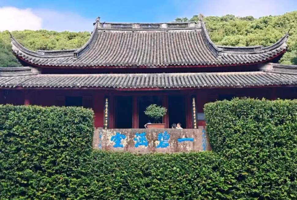 Baoguo Temple,Ningbo,Chinatour Traditional Chinese temple/pavilion with ornate tiled roofs and red walls, backed by greenery and a blue-character stone plaque in front.