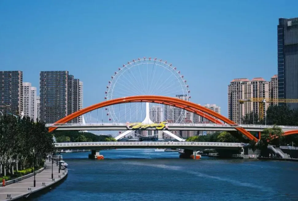 Tianjin Eye Ferris Wheel,Tianjin,Chinatour Orange arch bridge crosses a blue river with a ferris wheel and city skyline in the background.