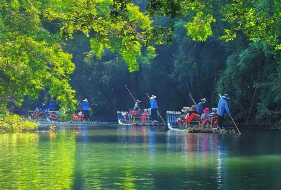 Nine-Bend Stream,Nanping,Chinatour Group of people in red life jackets ride bamboo rafts down a calm, green river guided by polesmen in blue shirts.
