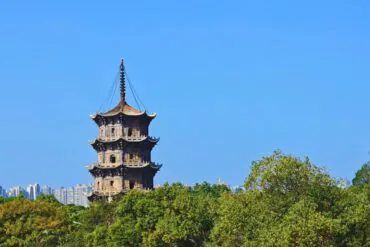 Kaiyuan Temple and West Street,Quanzhou,Chinatour Ancient multi-tier pagoda rising above green trees with a city skyline in the distance under a clear blue sky.