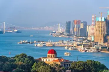 Gulangyu Island,Xiamen,Chinatour Harbor cityscape with a red-domed building in the foreground, blue water, and modern high-rrise skyline in the background.