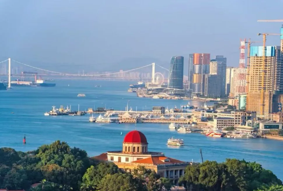 Gulangyu Island,Xiamen,Chinatour Harbor cityscape with a red-domed building in the foreground, blue water, and modern high-rrise skyline in the background.