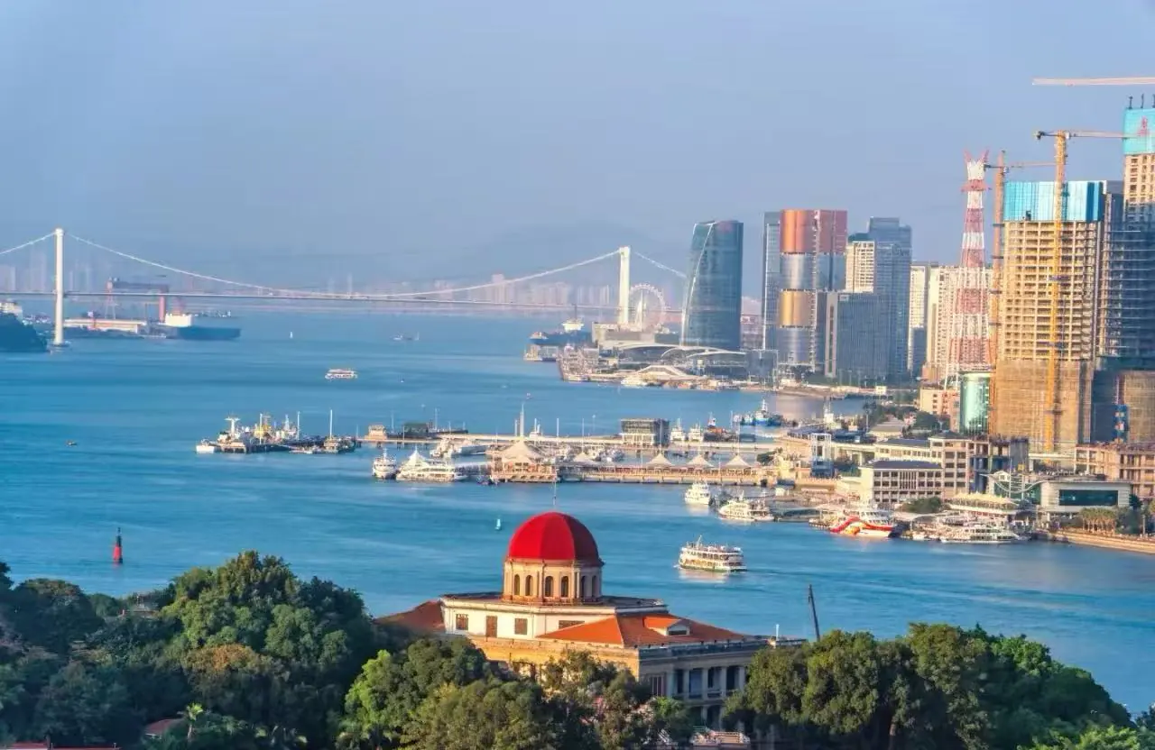 Harbor cityscape with a red-domed building in the foreground, blue water, and modern high-rrise skyline in the background.