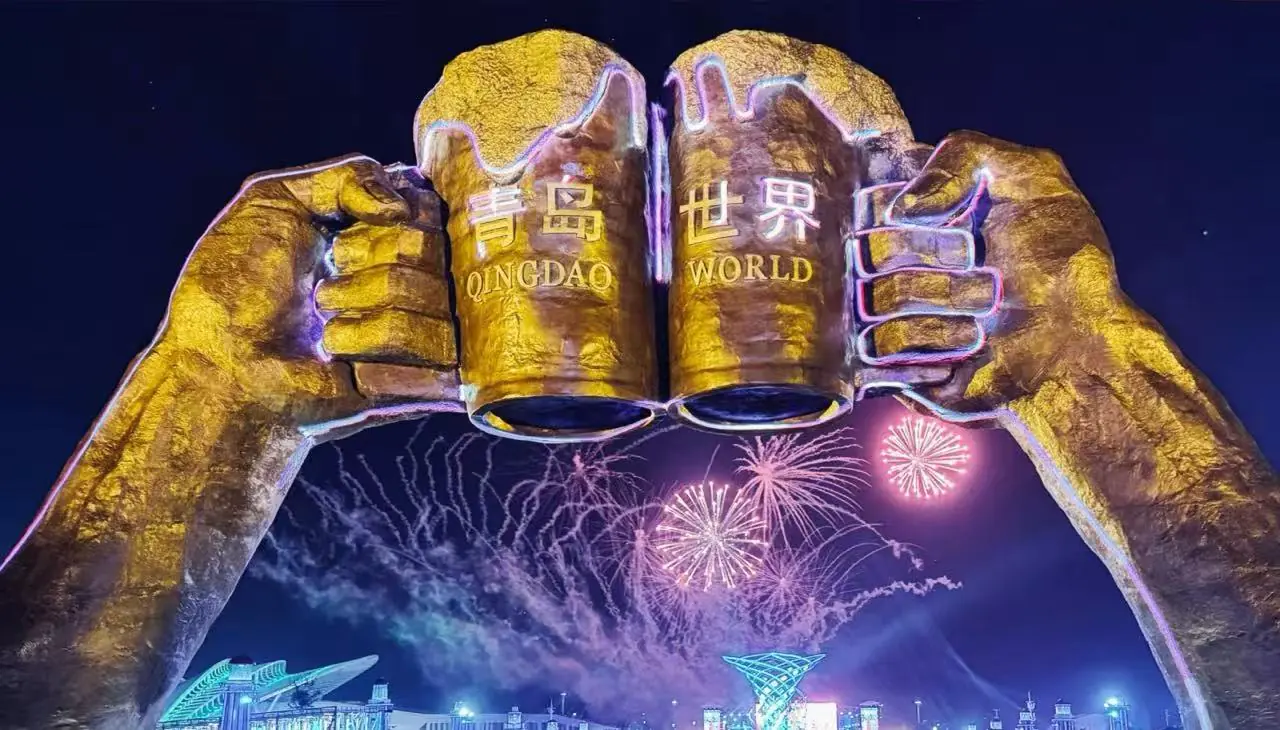 International Beer City,Qingdao,Chinatour Night view of giant golden fists forming an arch with the words 'QINGDAO WORLD' and colorful fireworks above a lit cityscape outside the venue.