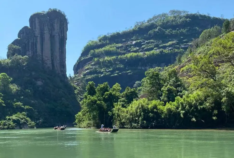 Wuyi Mountain UNESCO Site,Nanping,Chinatour Narrow river through a lush canyon with a tall rock pillar on the left and small boats on the water.