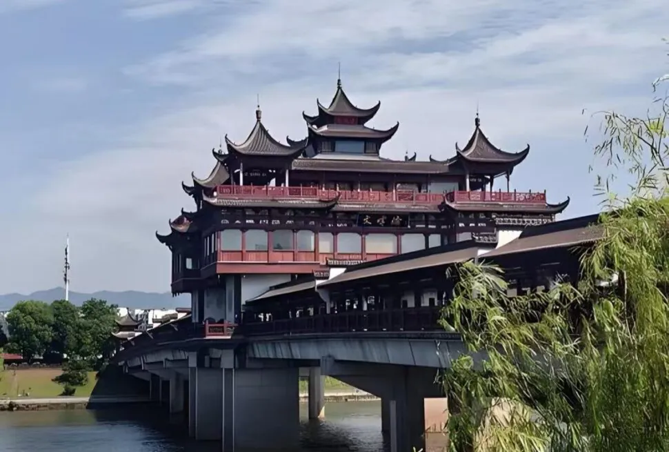 Tunxi Ancient Street,Huangshan,Chinatour Multi-story Chinese pagoda-style bridge crossing a calm river, with red railings and dark wooden eaves over water.