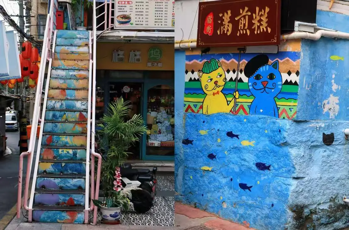 Colorful outdoor stairway beside a storefront, with a mural of two cats on a bright blue wall and a red sign above.
