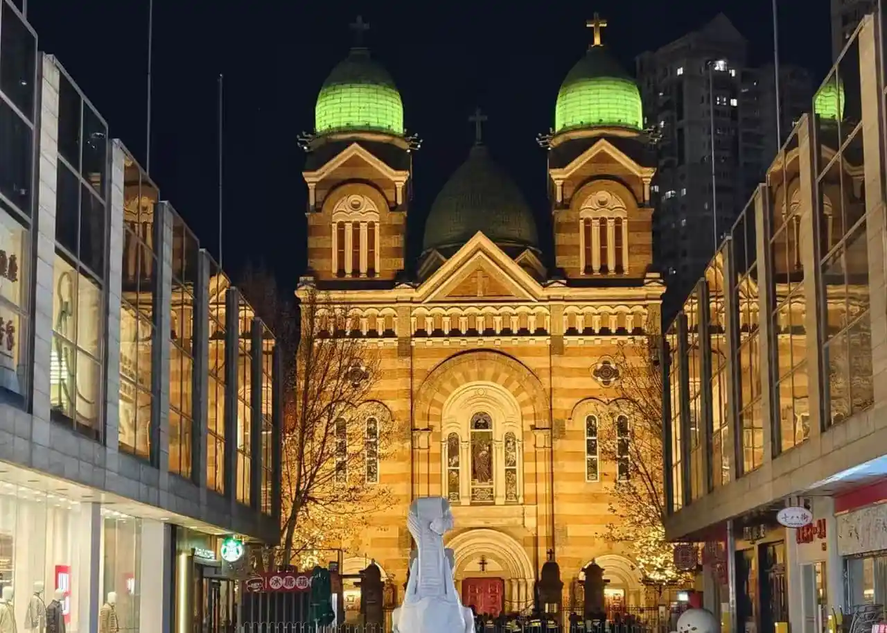 St. Joseph Cathedral Xikai Church,Tianjin,Chinatour Night view of a brick church with two green-domed towers at a busy city street, framed by glass storefronts and warm lights.