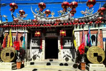 Shishi Ancient Town,Quanzhou,Chinatour Front view of a Chinese temple entrance adorned with red lanterns, dragon sculptures, and decorative banners along the roof.