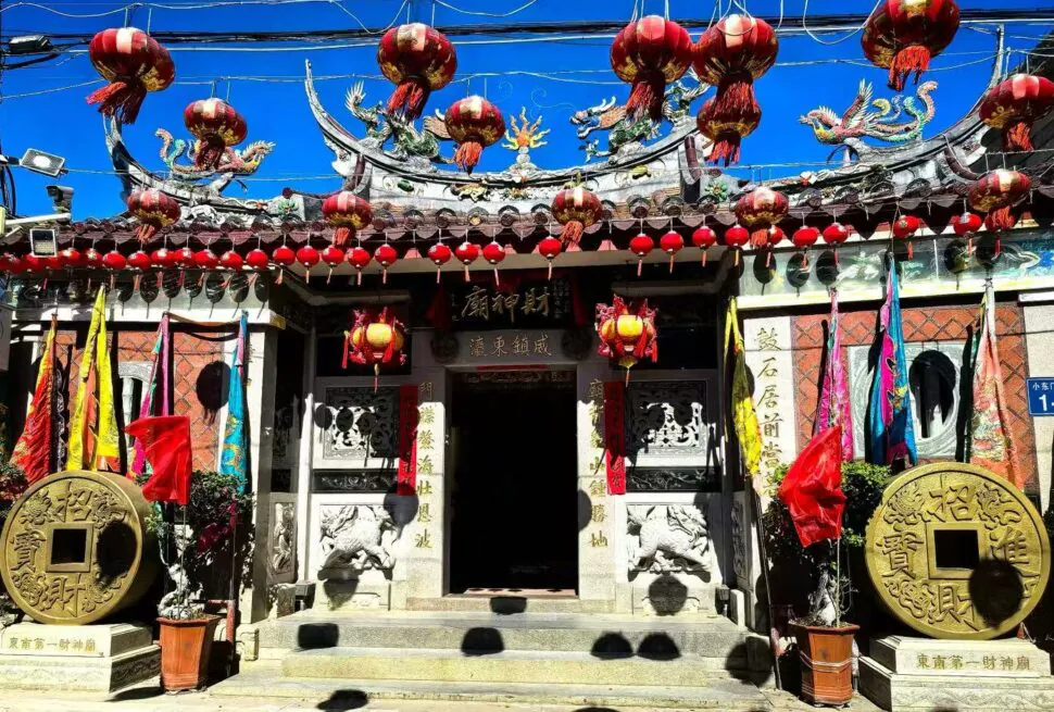 Shishi Ancient Town,Quanzhou,Chinatour Front view of a Chinese temple entrance adorned with red lanterns, dragon sculptures, and decorative banners along the roof.