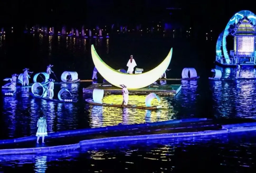 Nighttime water show with a glowing crescent moon float centerpiece and performers on floating platforms amid illuminated sculptures.Impression Sanjie Liu Show,Yangshuo,Guangxi,Chinatravel