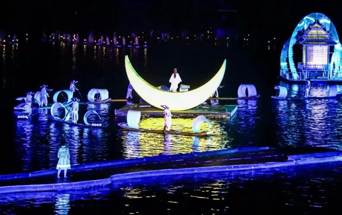 Nighttime water show with a glowing crescent moon float centerpiece and performers on floating platforms amid illuminated sculptures.Impression Sanjie Liu Show,Yangshuo,Guangxi,Chinatravel