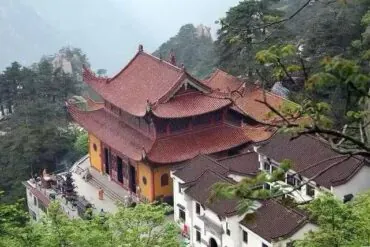 Yungu Temple,Huangshan,Chinatour Temple complex with red-tiled roofs perched on a hillside, surrounded by trees and misty mountains.