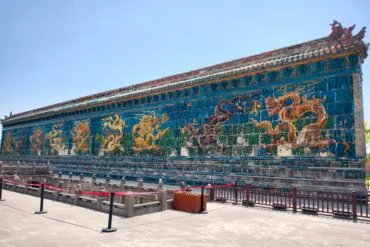 Datong Nine-Dragon Screen,Datong,Chinatour Colorful ceramic dragon mural along a blue-tiled wall at a Chinese temple, with a stone railing in the foreground.