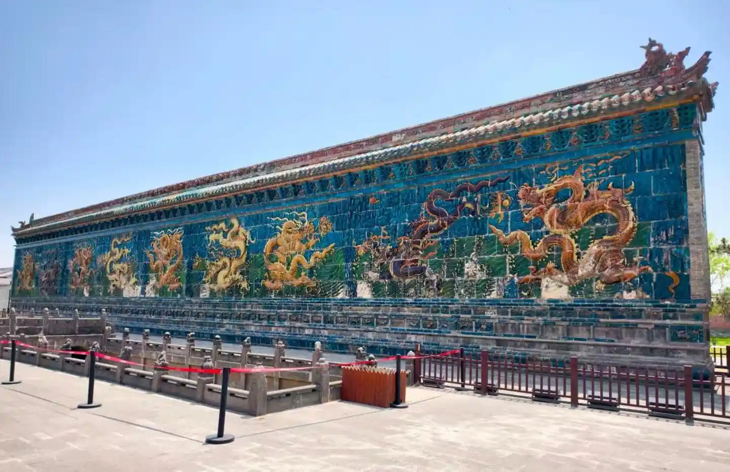 Datong Nine-Dragon Screen,Datong,Chinatour Colorful ceramic dragon mural along a blue-tiled wall at a Chinese temple, with a stone railing in the foreground.