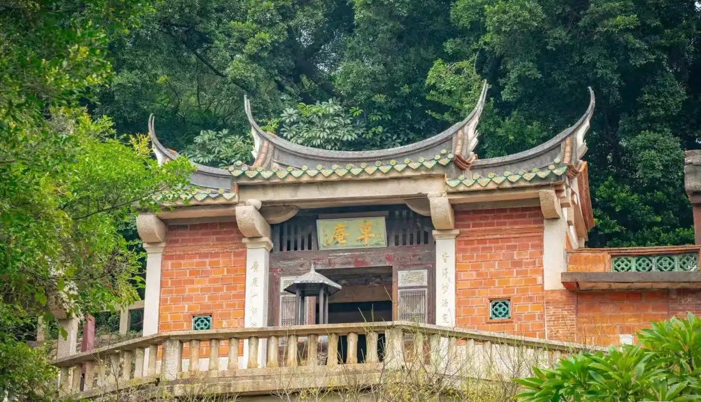 Grass Hut Manichaeism Site ,Quanzhou,Chinatour Traditional Chinese temple gate with curved tiled roof, red brick walls, and stone balustrade amid lush greenery