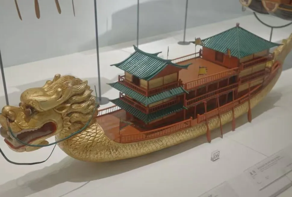 Quanzhou Maritime Museum,Quanzhou,Chinatour Ornate gold dragon-headed boat model with multiple teal-roofed pavilions on its back, displayed in a glass case.