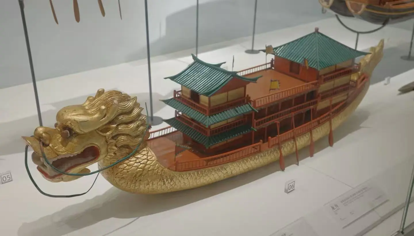 Quanzhou Maritime Museum,Quanzhou,Chinatour Ornate gold dragon-headed boat model with multiple teal-roofed pavilions on its back, displayed in a glass case.