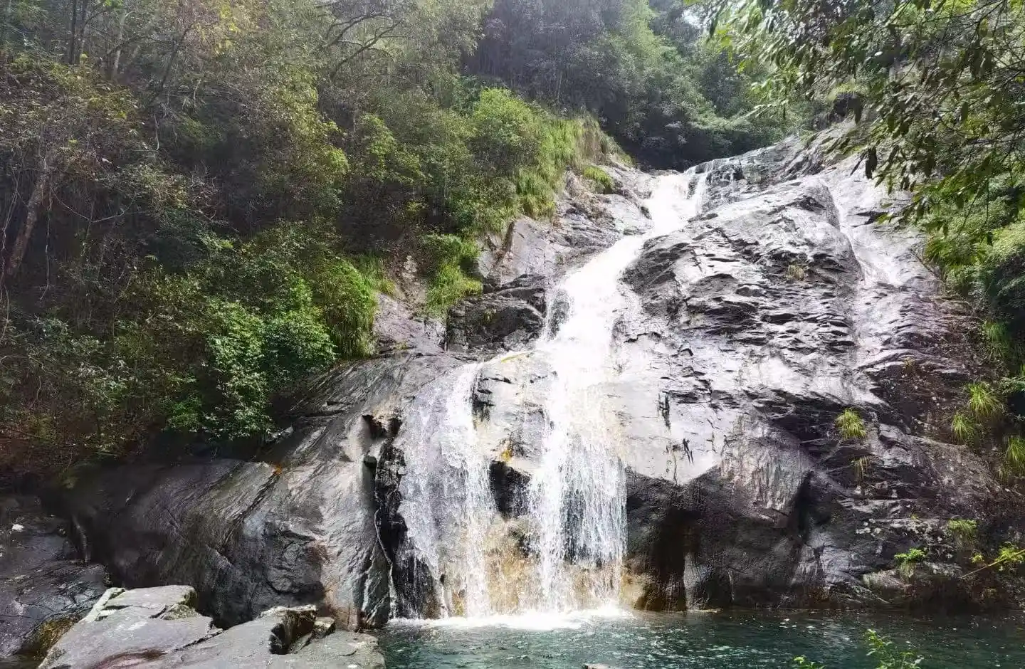 Huayan National Forest Park,Wenzhou,Chinatour Waterfall cascading down gray rocks into a tranquil pool, surrounded by dense green forest.