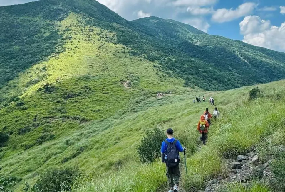 Mount Daiyun Scenic Area,Zhangzhou,Chinatour Hikers walking along a grassy mountain trail with blue sky and green hills in the background.
