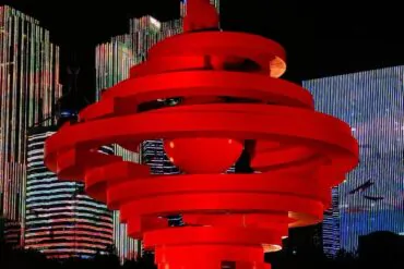 Qingdao May Fourth Square,Qingdao,Chinatour Red spiraling sculpture in a nighttime plaza with tall, brightly lit skyscrapers in the background and city lights.