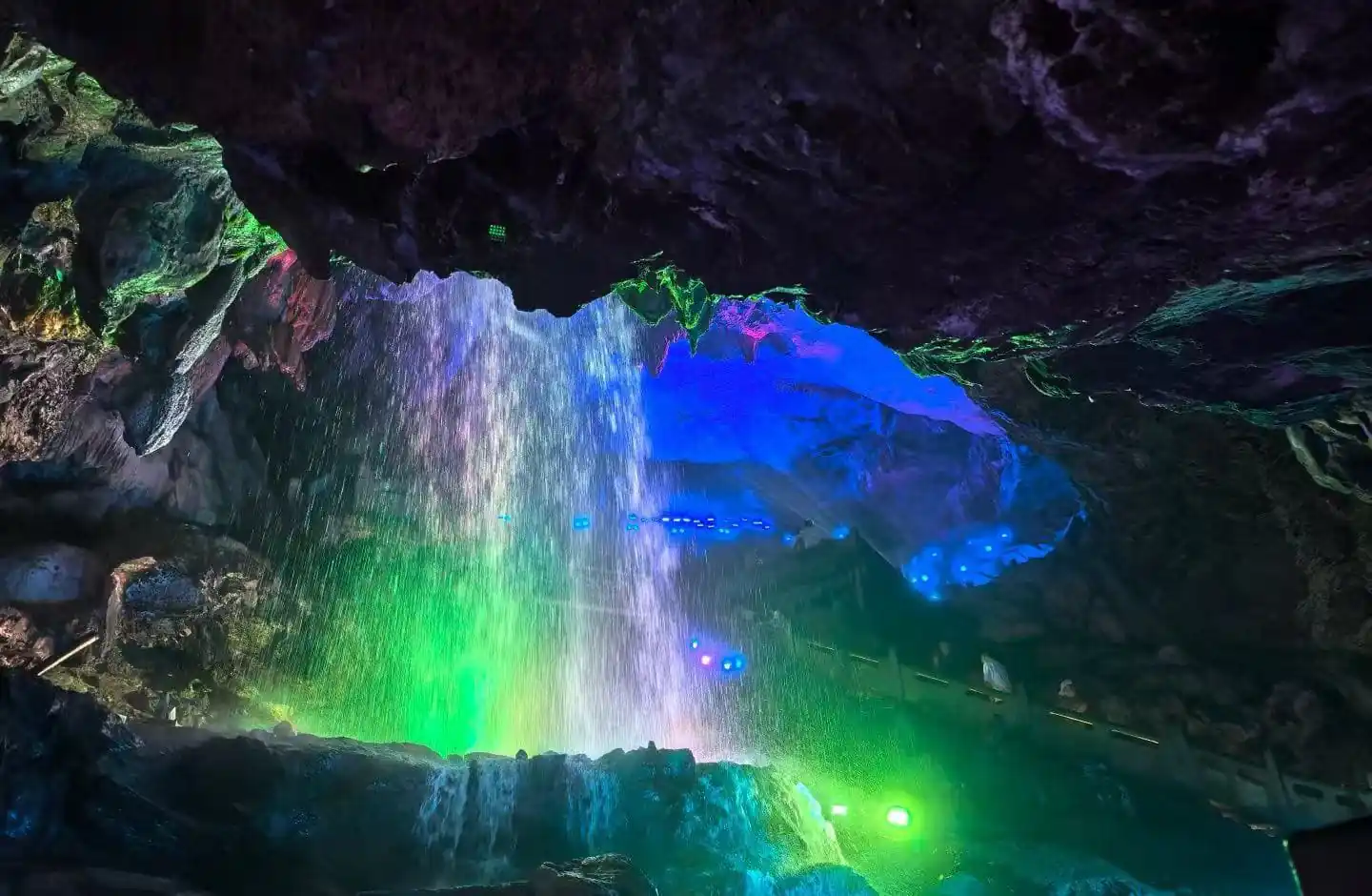 Shuanglong Cave ,Jinhua,Chinatour Cave interior with a colorful light show—green, blue, and purple glow on rocks and a waterfall mist.