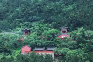 Mount Heng,Datong,Chinatour Red traditional temple buildings nestled in a lush green forest hillside on a slope with trees surrounding them.