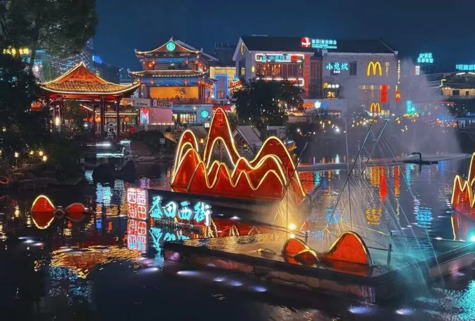 Nighttime river scene with glowing red neon mountain sculptures on the water and traditional Chinese architecture in the background.Yangshuo West Street,Yangshuo,Guangxi,Chinatravel
