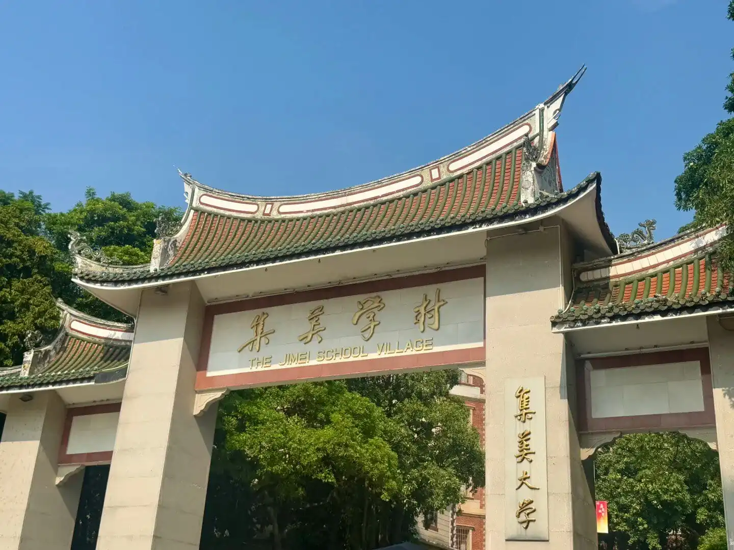 Jimei Educational Village,Xiamen,Chinatravel Entrance gate with traditional curved roof and gold inscription reading 'THE JIMEI SCHOOL VILLAGE' against a blue sky and green trees behind.