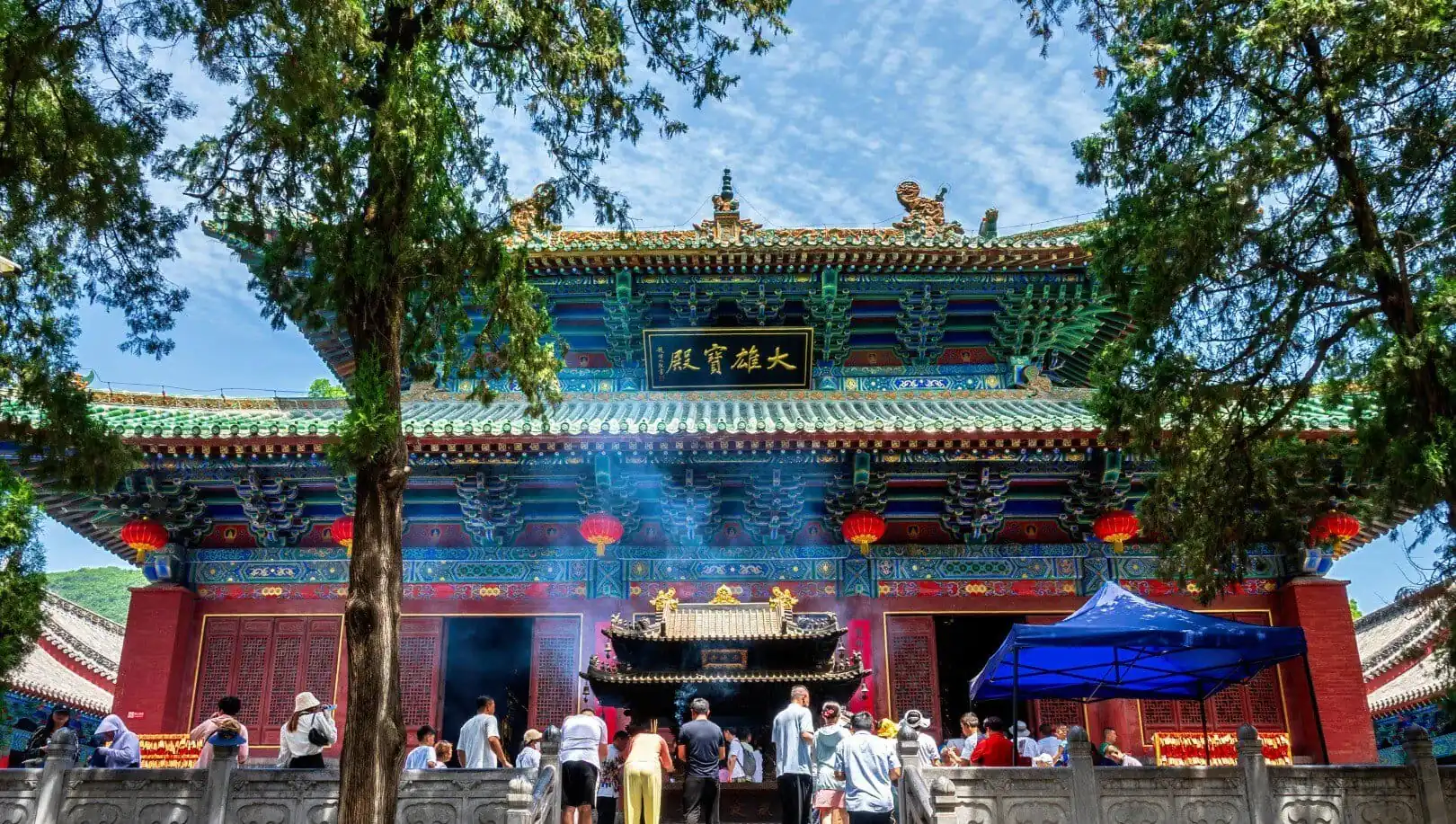 Ornate Chinese temple facade with a teal roof, red walls, hanging red lanterns, and worshippers at the front altar, smoke rising from incense.Songshan (Song Mountains) Scenic Area,Shaolin & Songshan Area,Henan,Chinatravel