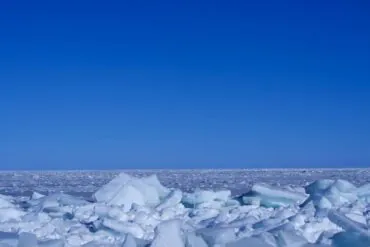 Ice-covered shore with jagged white ice chunks under a clear blue sky, Arctic horizon in the distance.Qinghai Lake,Xining,Qinghai