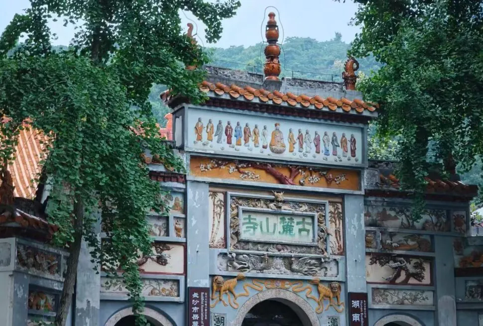 Ornate temple gate with gray stone walls, colorful murals of Buddhist figures, and trees framing the scene.Lushan Templen,Changsha,Hunan ,Chinatravel