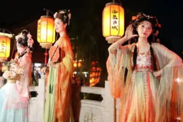 Luoyi Ancient City,Luoyang,Chinatour Three women in colorful traditional Chinese hanfu outfits posing with glowing lanterns at night festival on a stone railing.