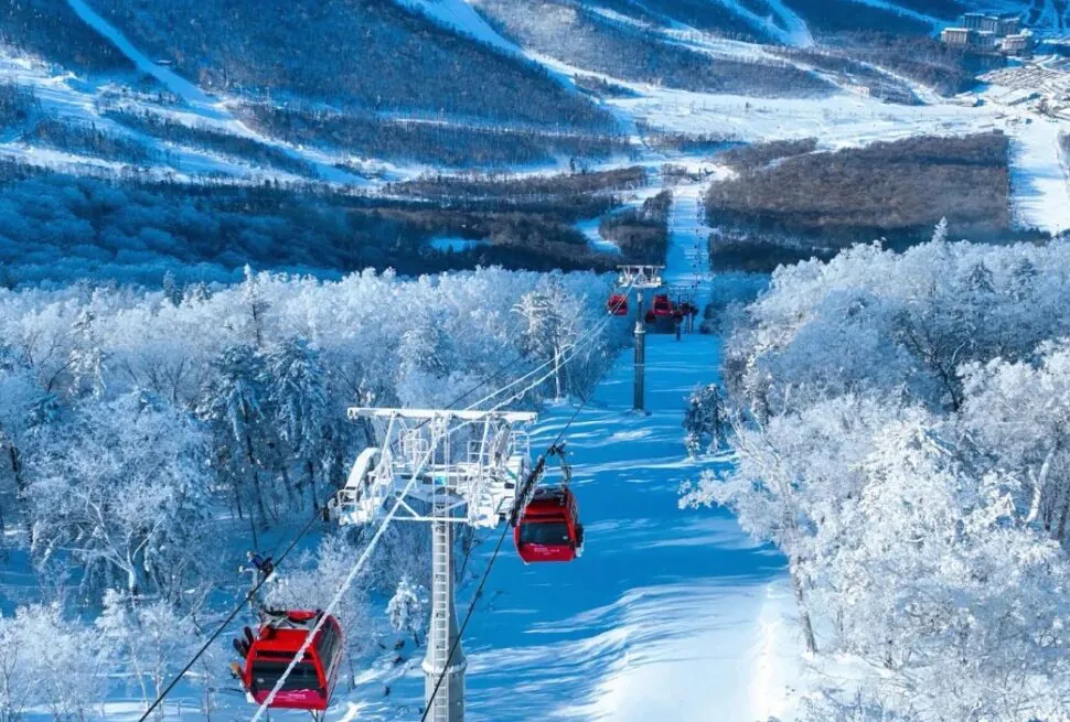 Snow-covered mountains and a ski lift with red gondolas gliding above a snow-blanketed forest.Jilin Beidahu Ski Resort,Chinatravel