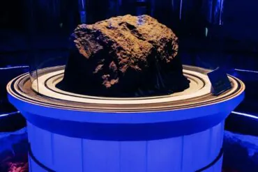 Rough brown rock displayed on a white circular pedestal under blue museum lighting within a glass display case.Jilin City Museum,Chinatravel