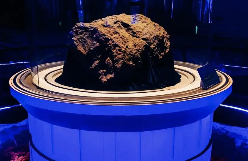 Rough brown rock displayed on a white circular pedestal under blue museum lighting within a glass display case.Jilin City Museum,Chinatravel