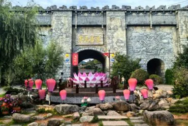 Puge Tea Horse Road Adventure,Shangri-La,Chinatour Stone fortress gate with arched entrance, Chinese-sign plaque, surrounded by pink lotus lanterns and a large pink lotus sculpture.