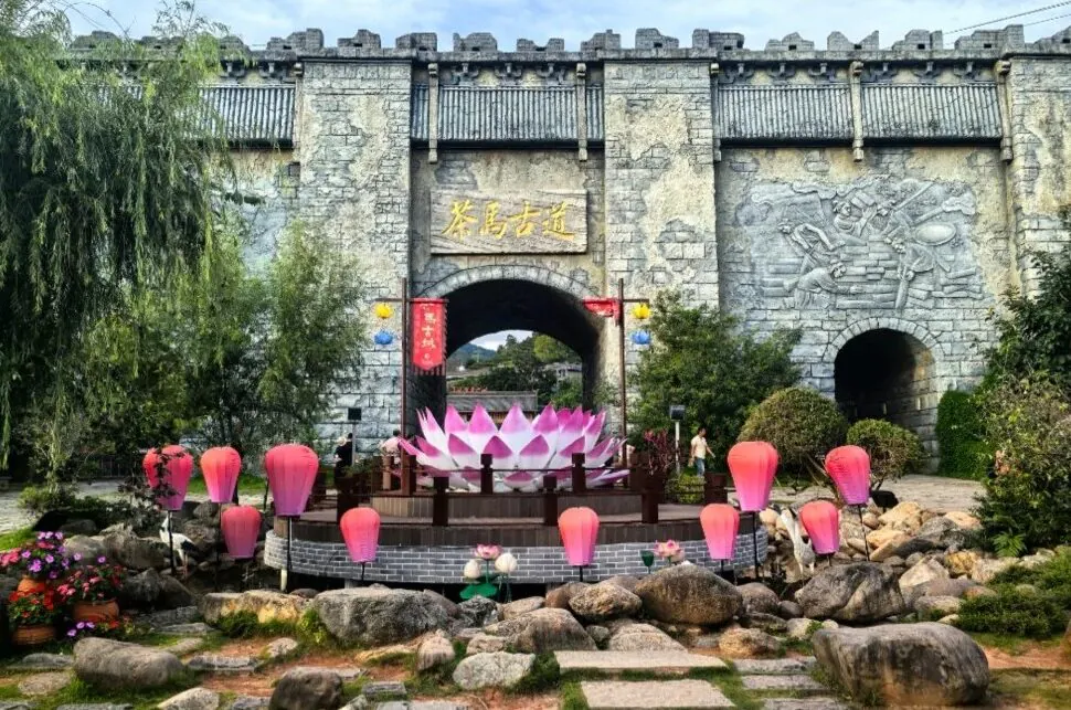 Puge Tea Horse Road Adventure,Shangri-La,Chinatour Stone fortress gate with arched entrance, Chinese-sign plaque, surrounded by pink lotus lanterns and a large pink lotus sculpture.
